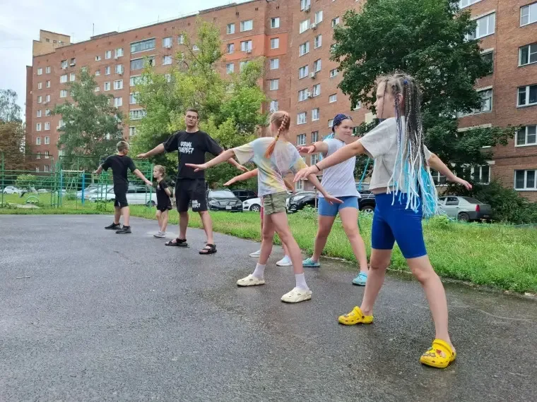 Группа жителей 43-го дома на проспекте Кулакова выполняет утреннюю зарядку под руководством преподавателя на открытой спортплощадке во дворе.