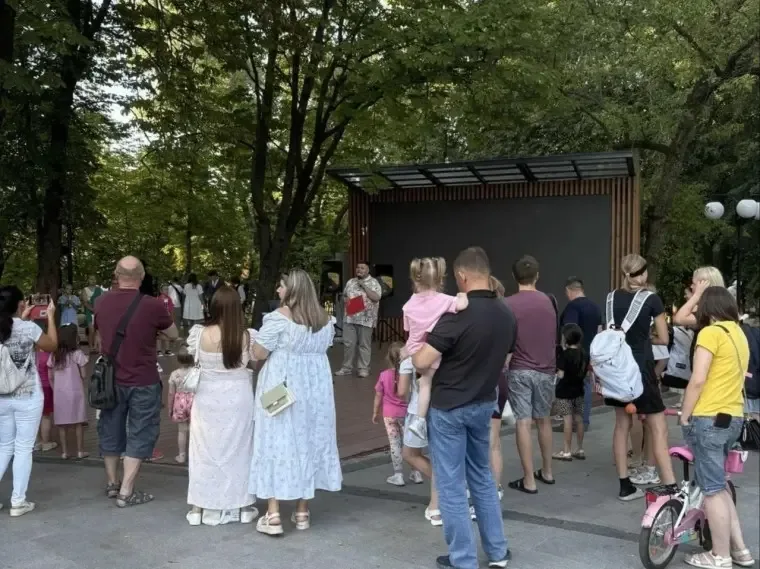 Дети в ярких костюмах танцуют на сцене в летнем парке перед зрителями