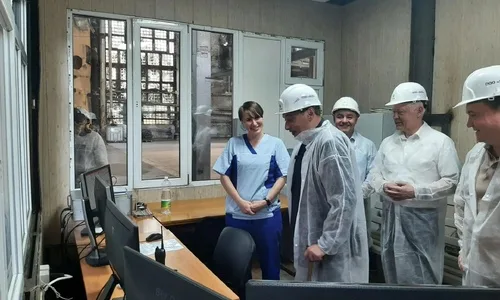 Александр Хинштейн на фоне сахарного завода, обсуждающий процесс переработки свеклы с работниками предприятия.