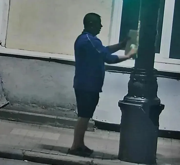 Мужчина расклеивает объявления на стене в центре Курска, на фоне городской архитектуры.